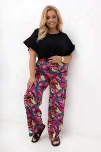 Spodnie damskie plus size Marisa z szerokimi nogawkami i egzotycznym owocowym wzorem. Model prezentuje wygodny fason z gumką w pasie i kieszeniami w codziennej stylizacji.