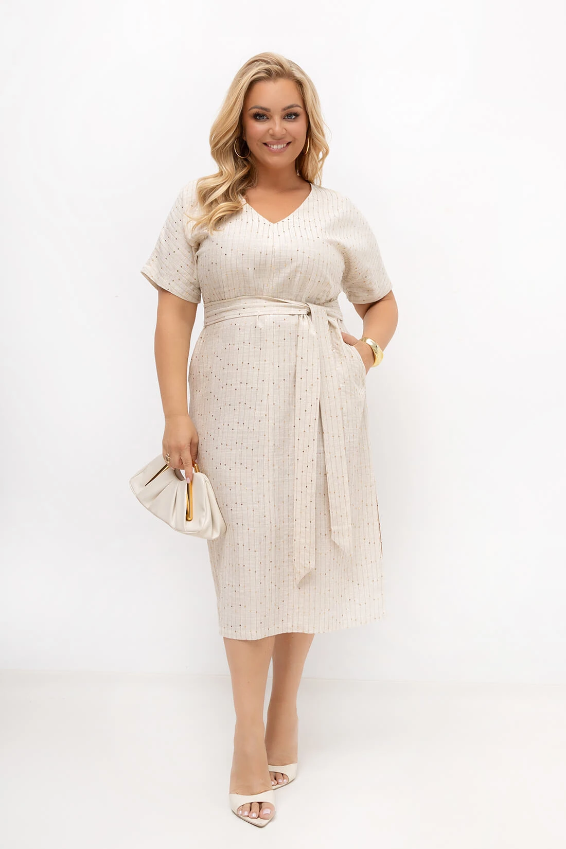 Beżowa sukienka plus size przewiązana paskiem podkreślającym talię. Dekolt V, subtelne cekiny oraz minimalistyczny fason sprawiają, że model doskonale sprawdzi się na rodzinne uroczystości i letnie wyjścia.
