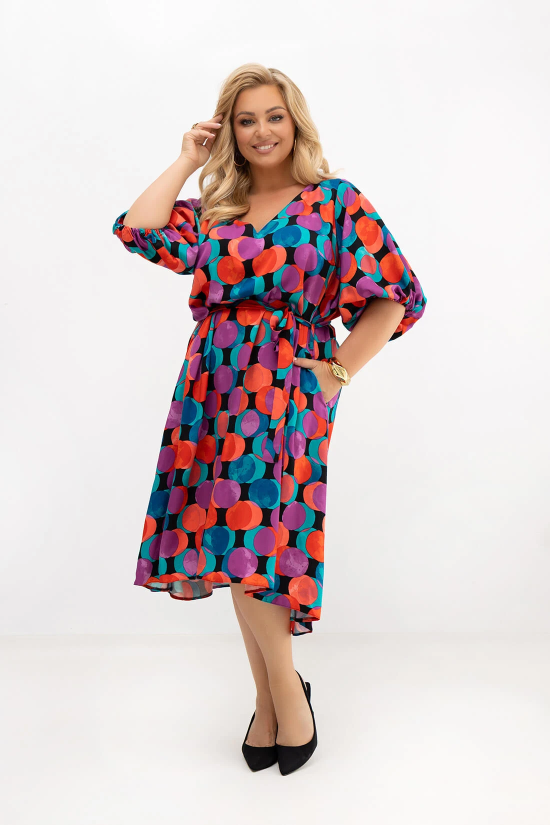 Sukienka plus size Arie w kolorowe koła prezentowana z przodu. Dekolt V, pasek podkreślający talię, bufiaste rękawy oraz kieszenie tworzą wygodny i kobiecy model idealny na lato.