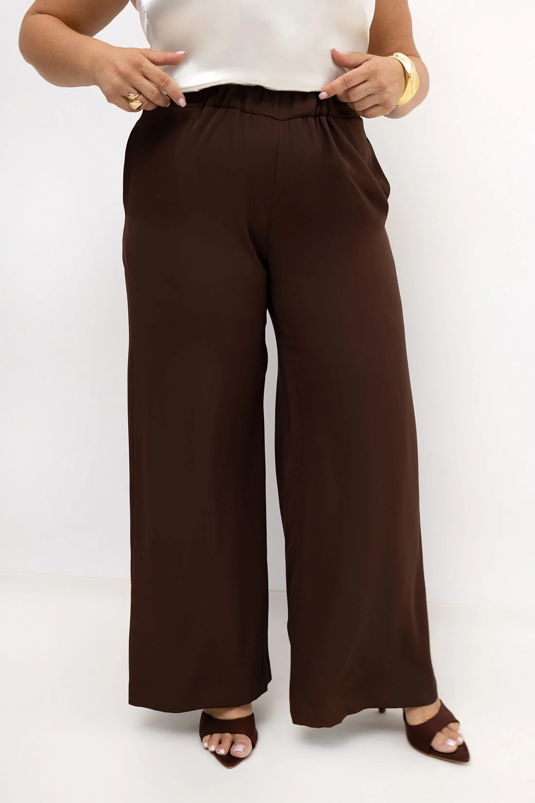Brązowe eleganckie spodnie damskie Elisa PLUS SIZE z szeroką prostą nogawką. Elastyczny pas z gumką zapewnia wygodne dopasowanie do sylwetki, a klasyczny fason sprawdzi się zarówno na co dzień, jak i do eleganckich stylizacji.